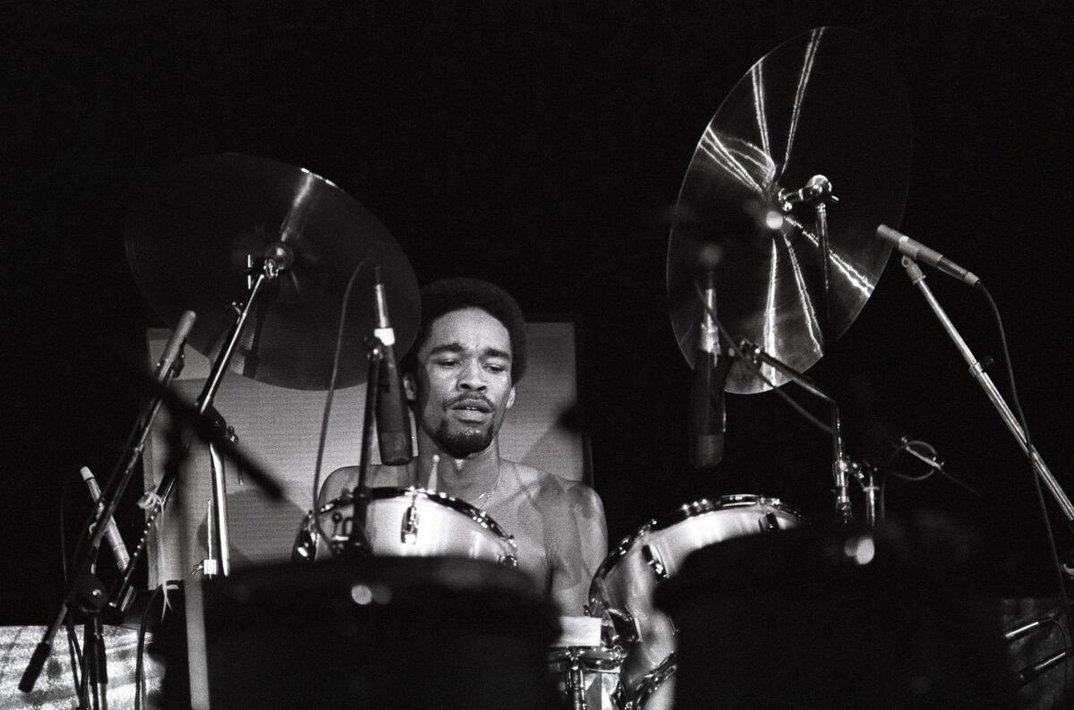 A black-and-white photo of a man playing drums onstage.
