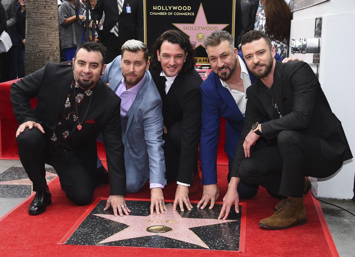 Chris Kirkpatrick, Lance Bass, JC Chasez, Joey Fatone and Justin Timberlake, all wearing suits, crouch by a Walk of Fame star