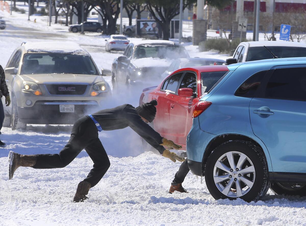 A man pushes free a car that spun out on a snow-covered road.