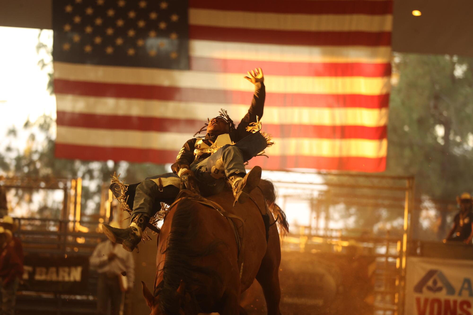A man rides a horse, with a giant American flag hanging behind him.