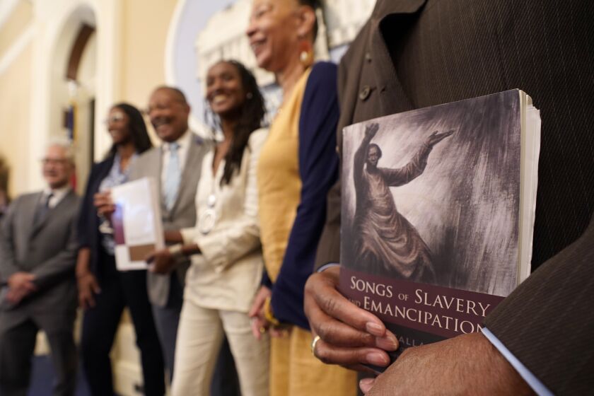 FILE—Dr. Amos C. Brown, Jr., vice chair for the California Reparations Task Force, right, holds a copy of the book Songs of Slavery and Emancipation, as he and other members of the task force pose for photos at the Capitol in Sacramento, Calif., on June 16, 2022. California's committee to study reparations for African Americans will meet in Oakland Wednesday, Dec. 14, 2022, to discuss requirements for residents who may receive some form of compensation. (AP Photo/Rich Pedroncelli, File)