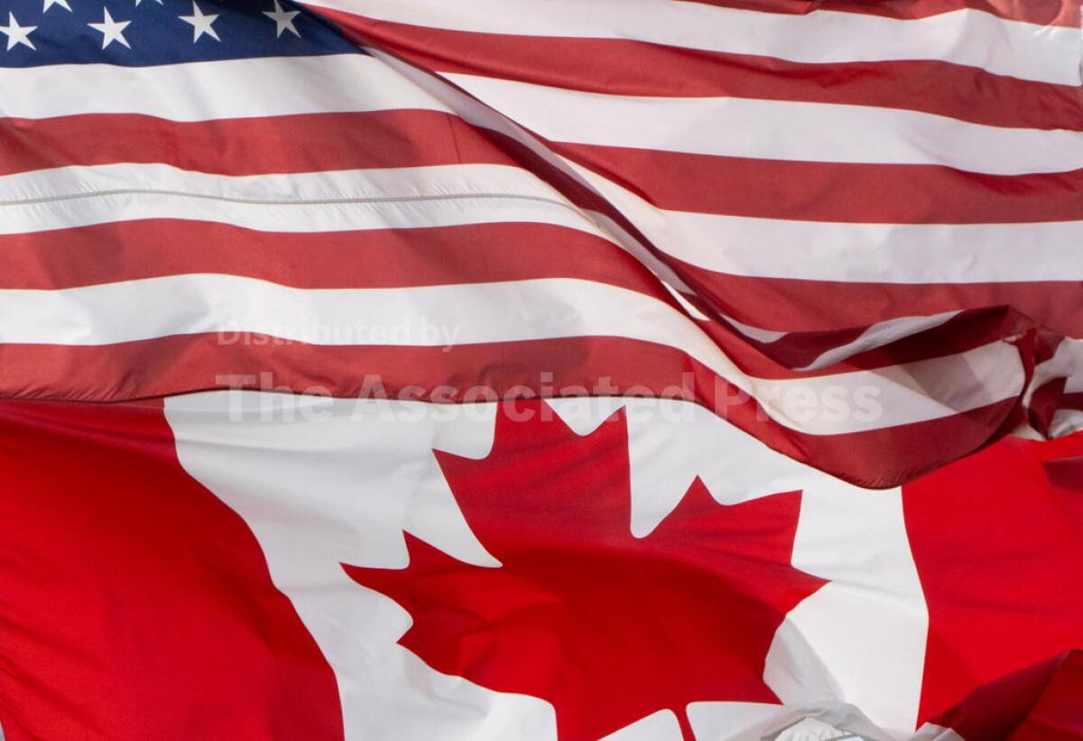 The flags of Canada and the U.S. fly close together.