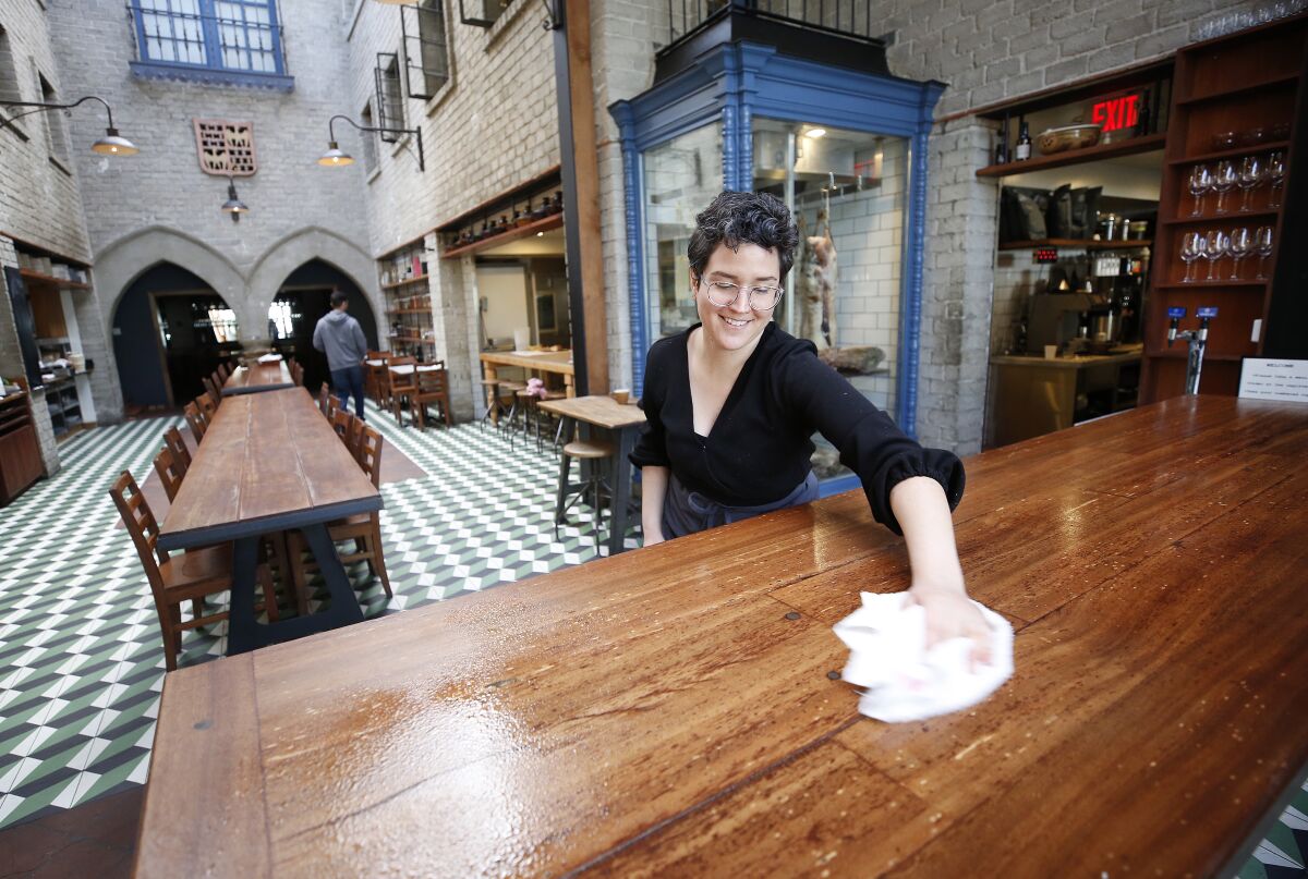 Restaurant manager Grace Curran wipes tabletops with disinfectant at Republique.