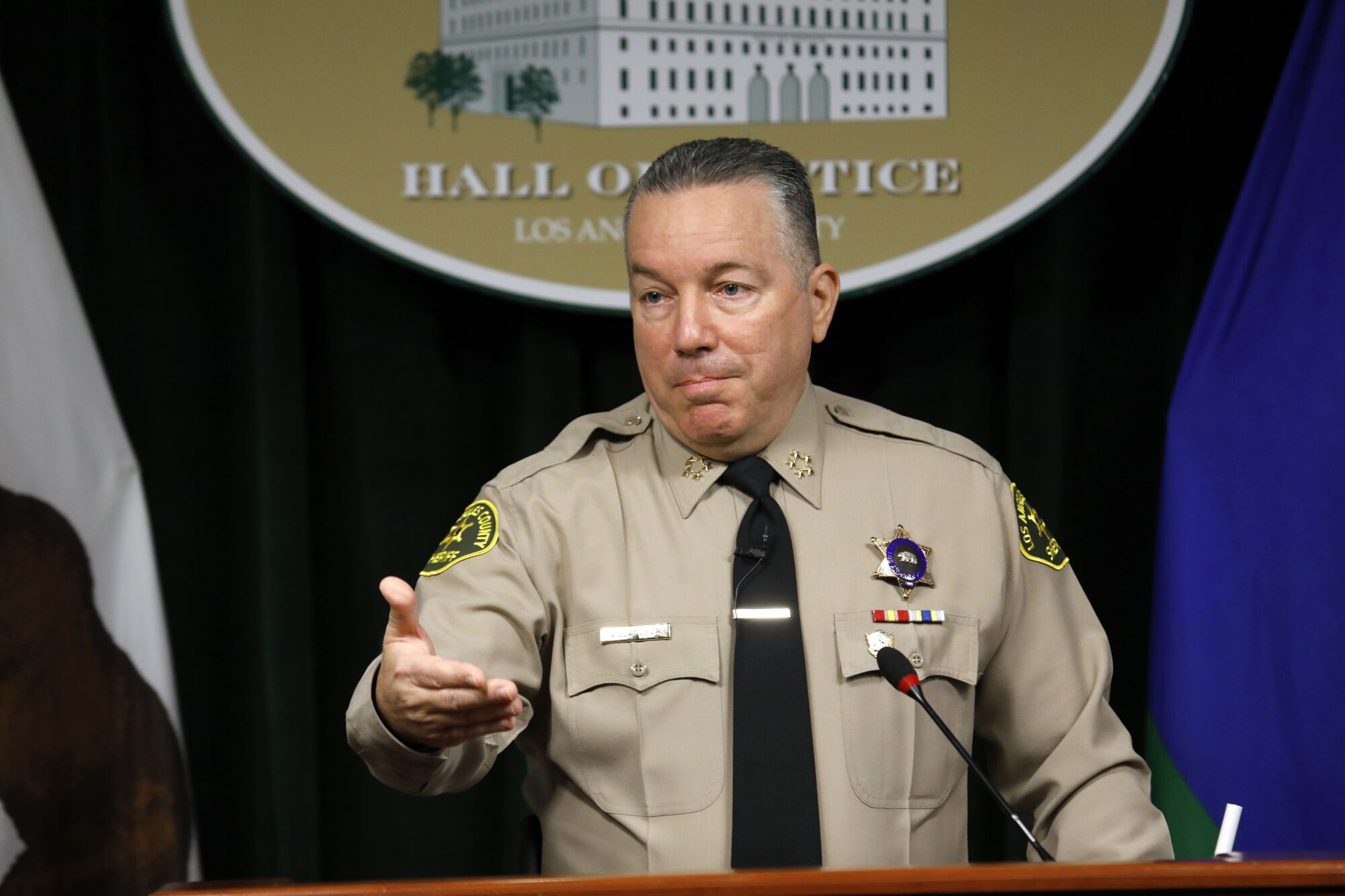 Alex Villanueva gestures with his right hand in front of a microphone