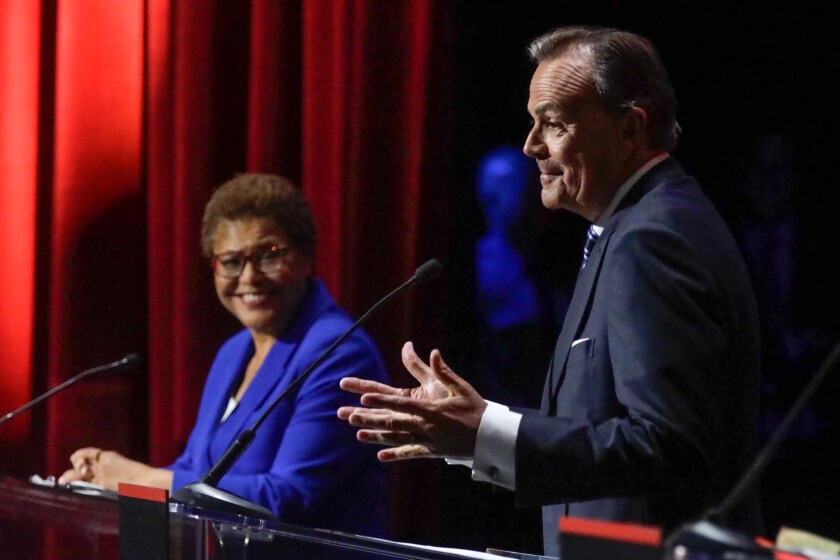 Rep. Karen Bass smiles as rival candidate Rick Caruso gestures during a mayoral debate.