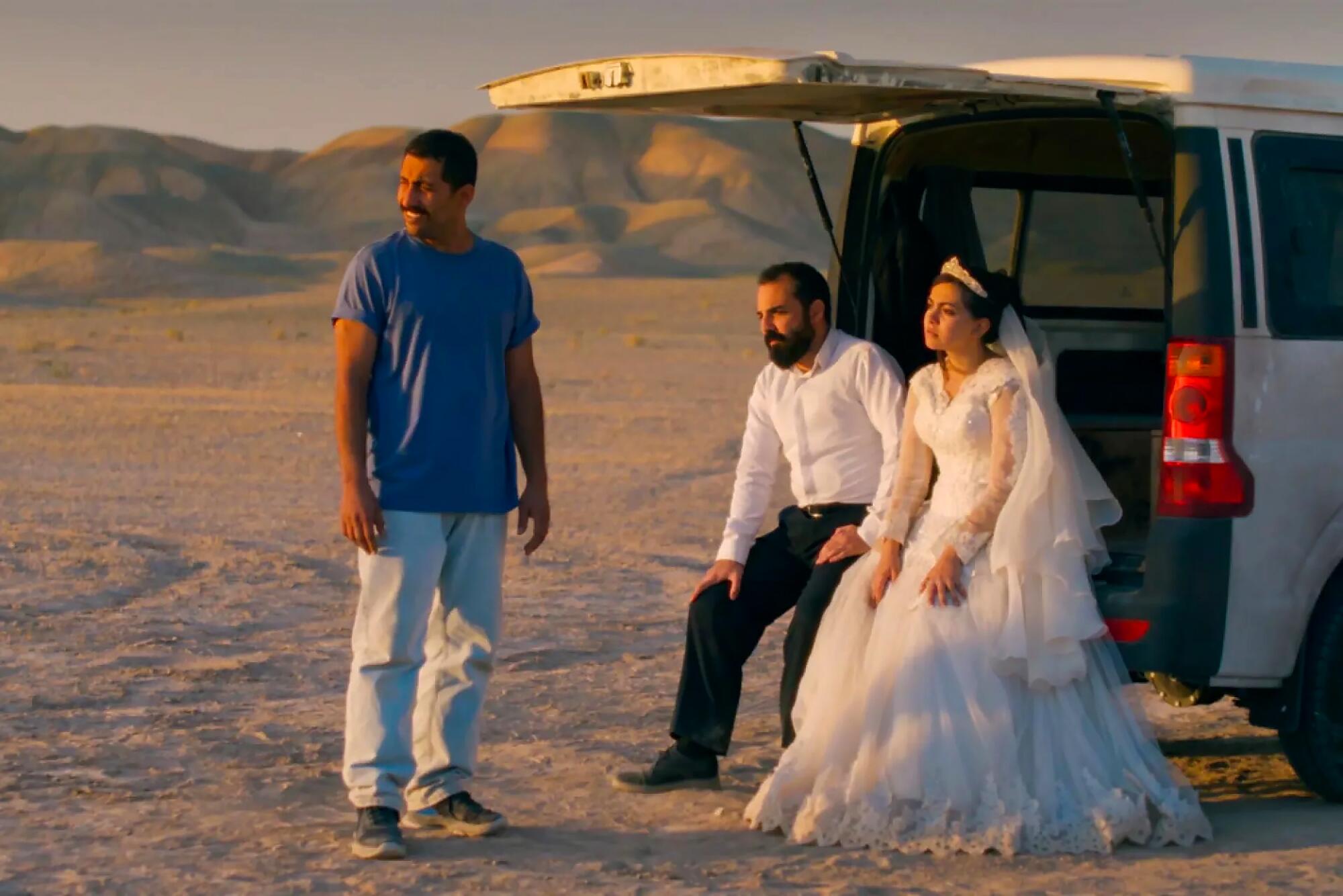 People sit on a van parked in a desert.