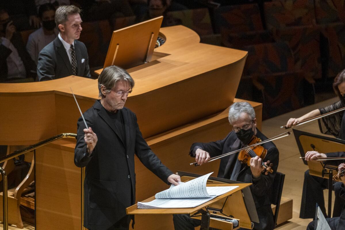 Conductor Esa-Pekka Salonen, wearing a dark suit, stands at a podium, before an organist and a violinist.