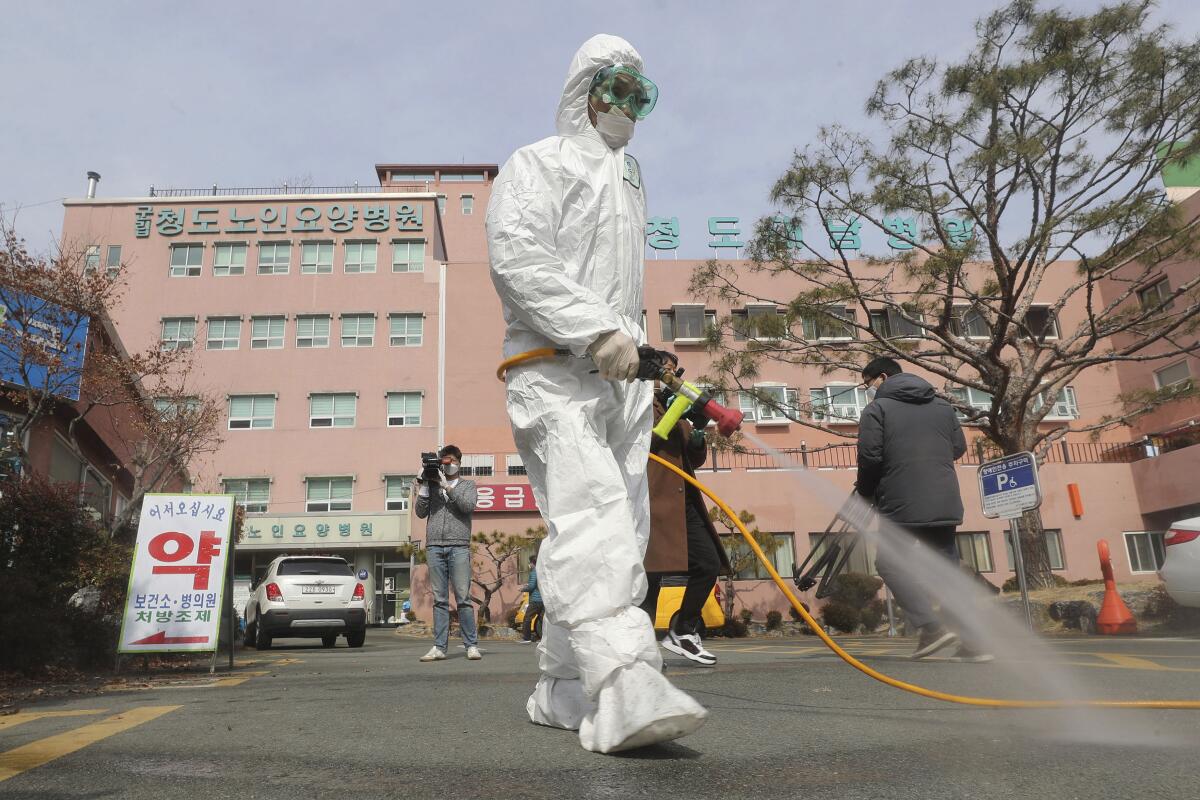 A worker in protective medical gear sprays disinfectant outside a South Korea hospital.