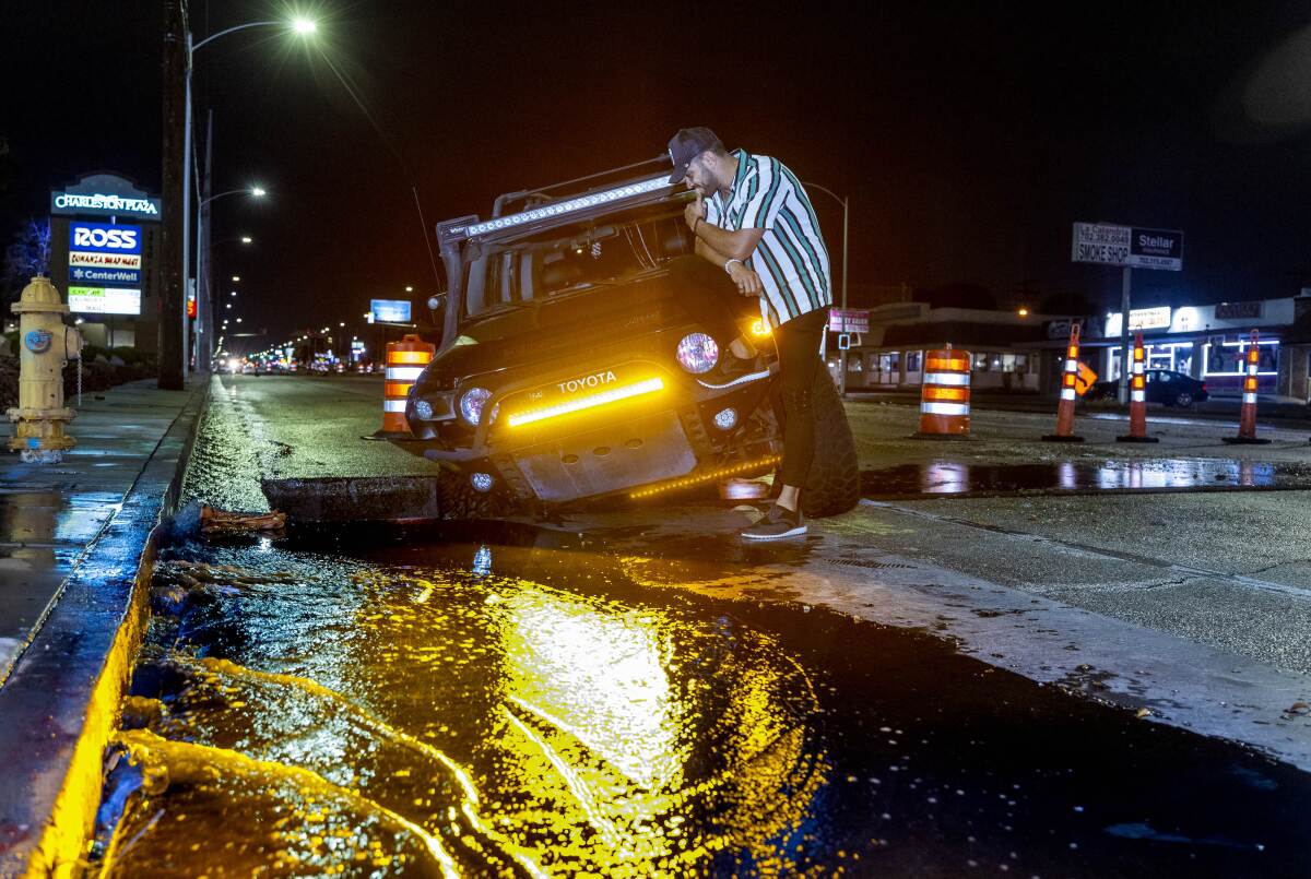 Driver Miguel Reyes checks out his vehicle stuck in a construction hole due to flooding in Las Vegas