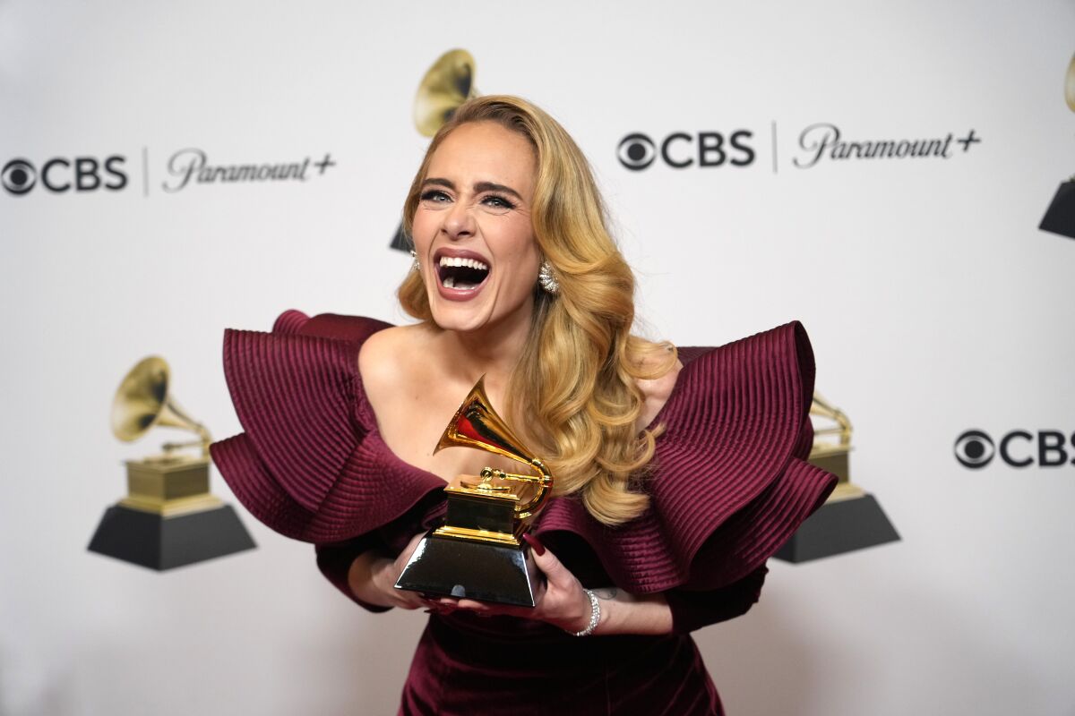 Adele leans forward with an open-mouth smile as she holds her Grammy Award trophy