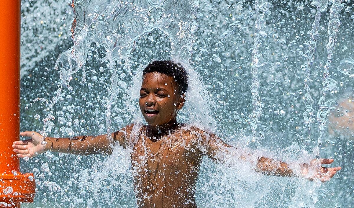 Majay Smith, 11, with arms outstretched, cools off at spray pool where water falls on him.