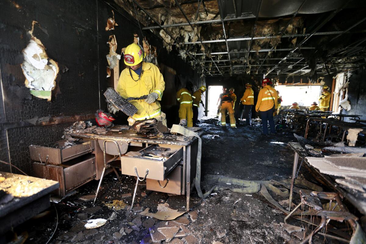 A Redlands firefighter inspects a melted computer keyboard while cleaning up a classroom that was allegedly set on fire at Redlands High School in Redlands on March 18.
