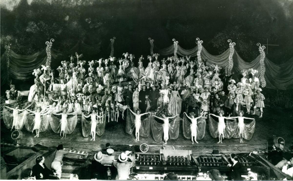 Rows of people in costume stand on an outdoor stage.