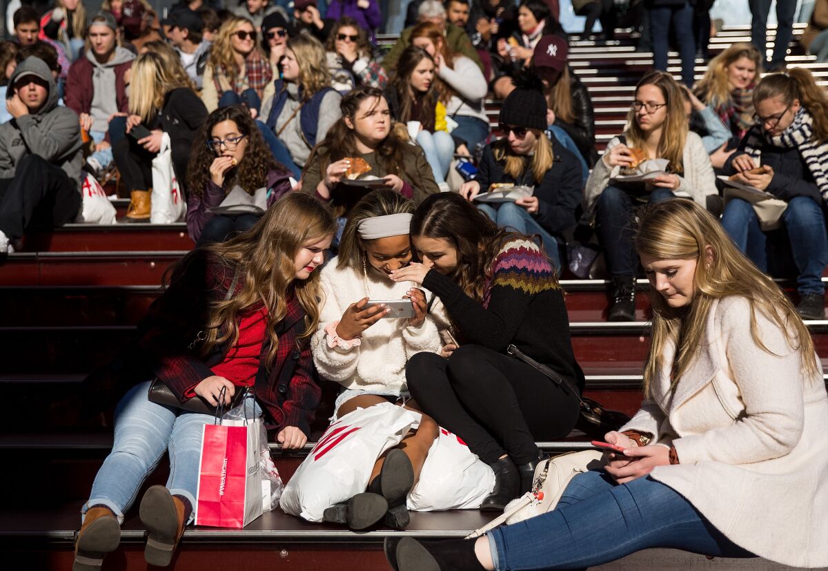 A group of teens look at a photographs on a smartphone in Times Square in New York City.