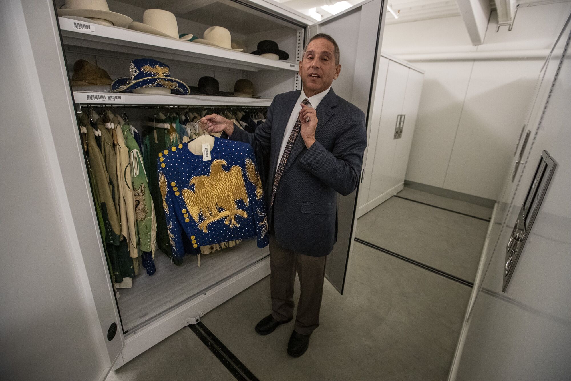 A man stands in front of a closet holding historic garments.