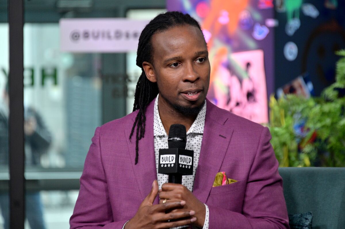A man in a suit jacket talks into a microphone as he is interviewed.