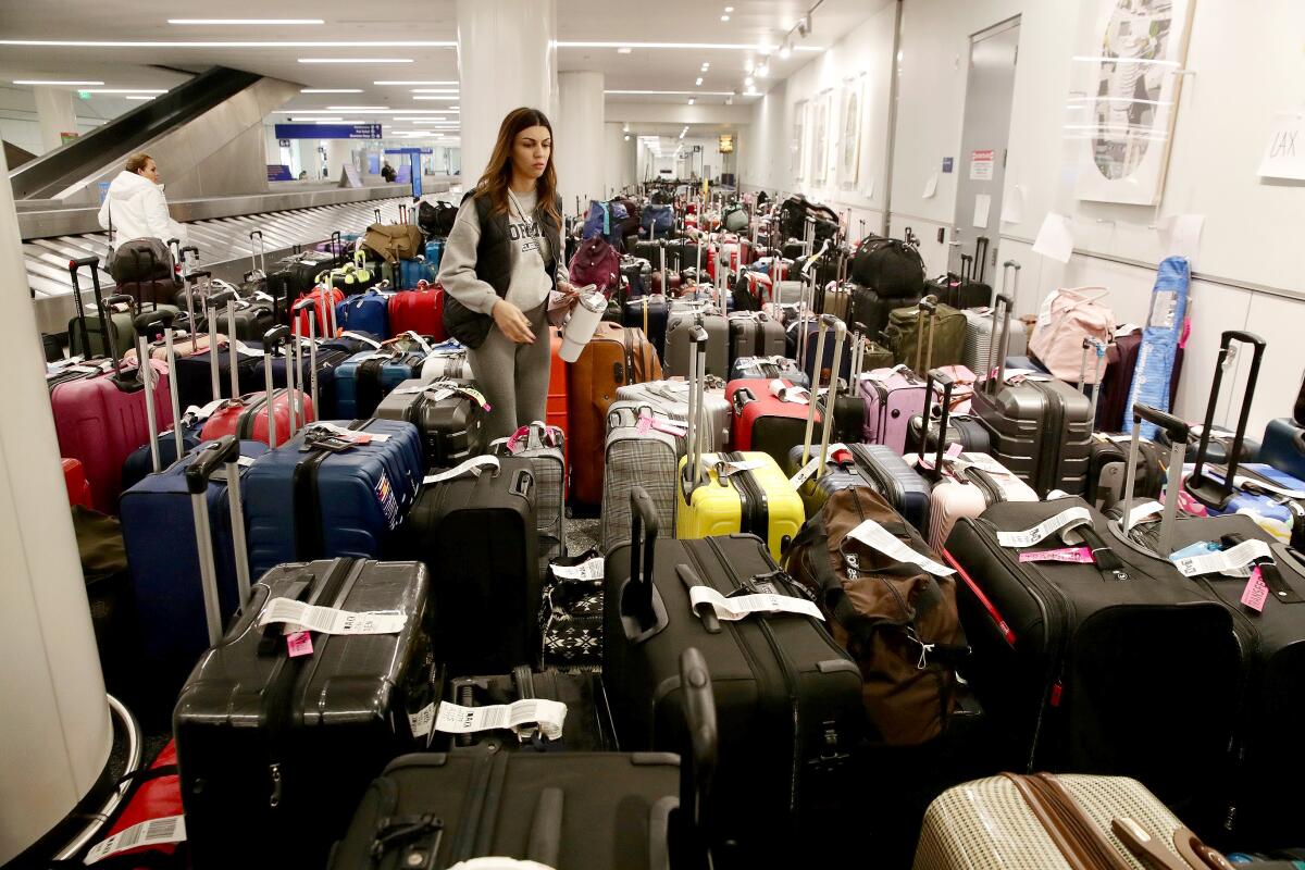 A passenger stands amid dozens of bags inside an airport terminal.
