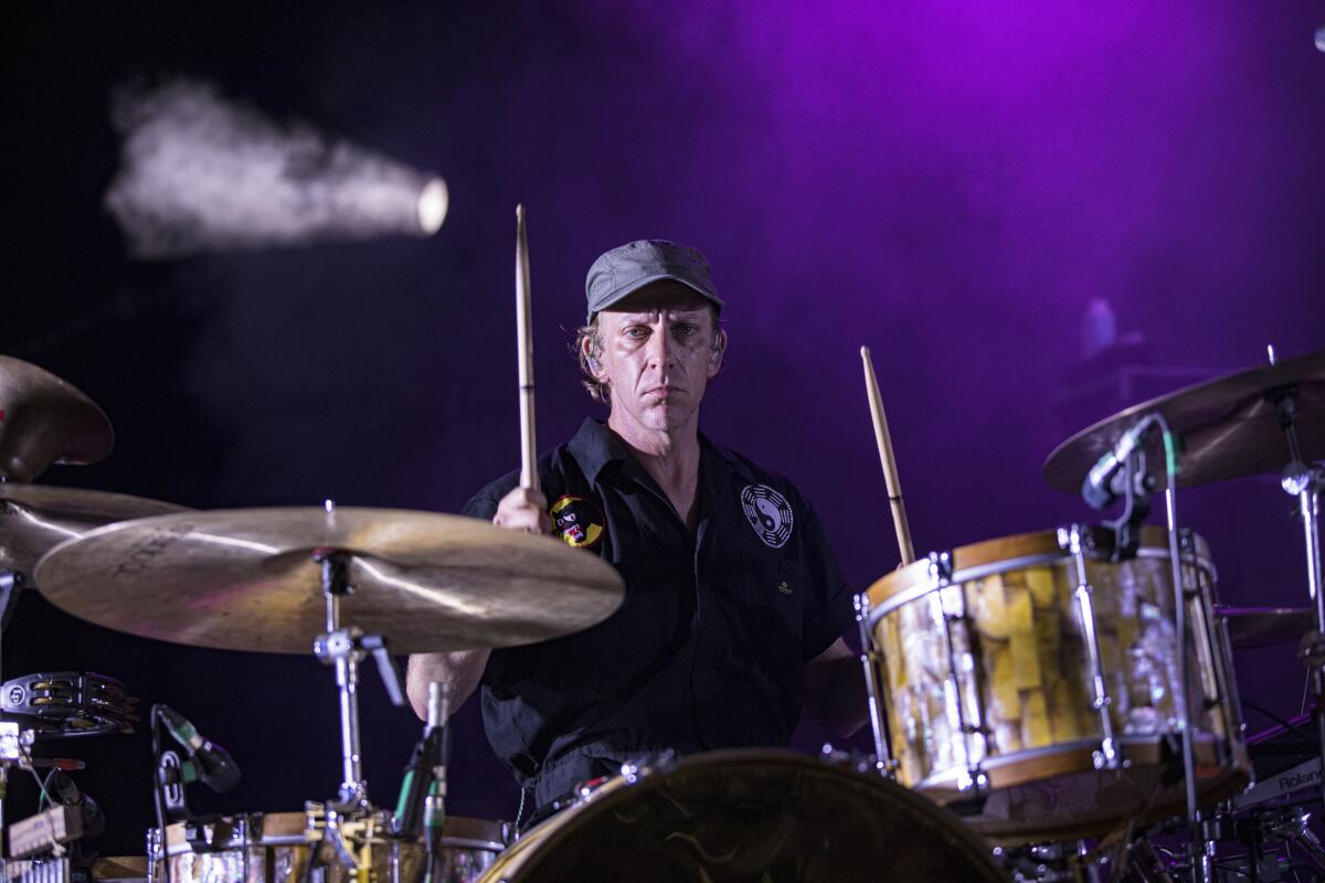 A man with a gray hat and black shirt plays the drums onstage.