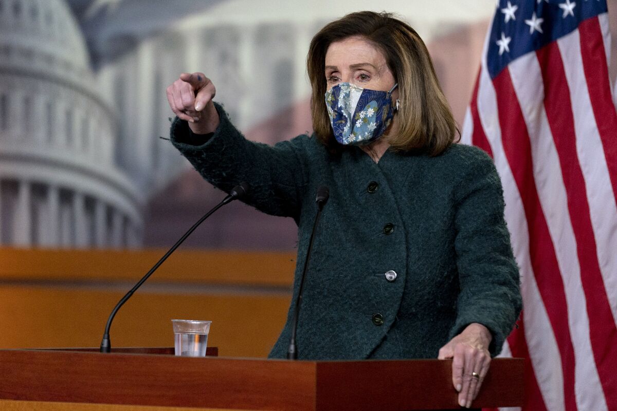 Nancy Pelosi, wearing a face mask, stands at a lectern.