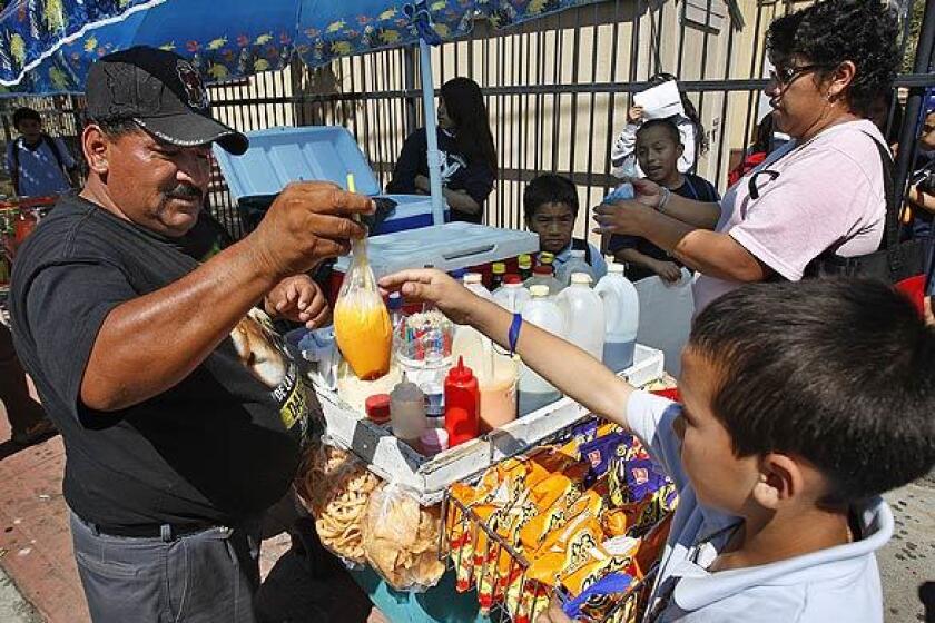 During his busiest time of the day, street vendor Amado Campos hands Kevin Tarot, 9, a bag of flavored shaved ice in front of Dolores Mission Catholic School in Los Angeles.