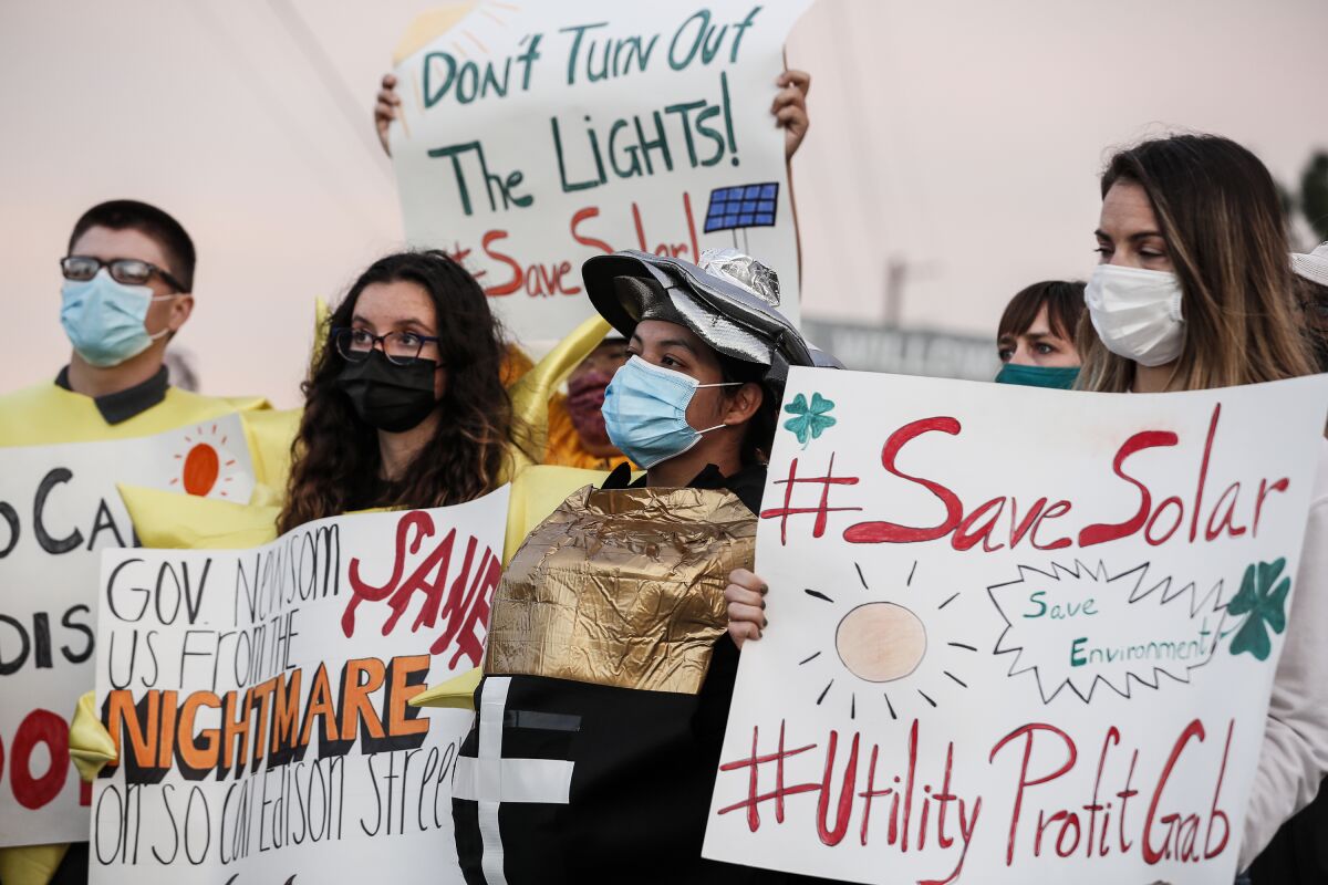 People in face masks hold signs, including one that says "#savesolar" and "UtilityProfitGrab"