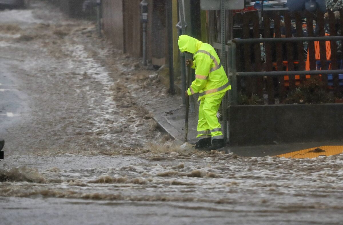 A city worker clears a drain at Jasmine and South Coast Highway during the storm Tuesday morning in Laguna Beach.