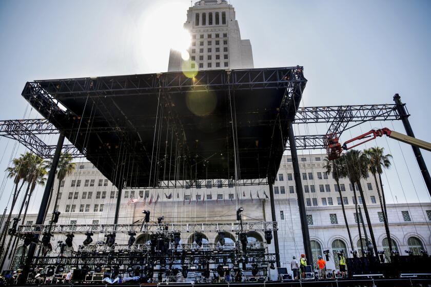 With Los Angeles City Hall in the background, crews work to set up equipment on a stage for this weekend's Made In America concert.