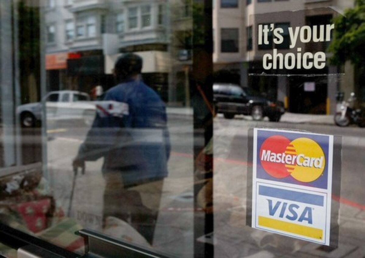 A man walks past a shop window displaying a MasterCard and Visa credit card sign.