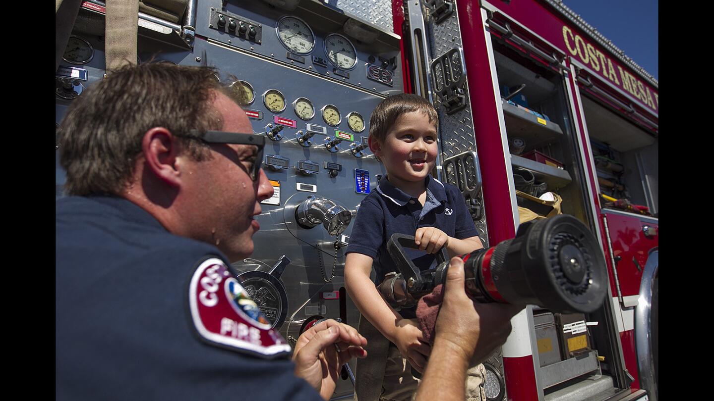 Travis Johnson, an engineer with the Costa Mesa Fire Department, shows Logan Castle, 4, how to work a firehose during Truck Adventures at the OC Fair & Event Center on Saturday.