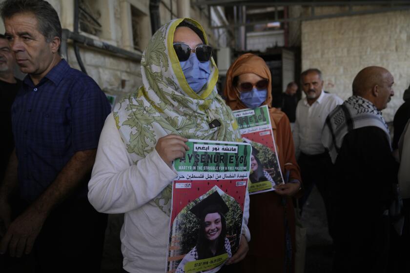 Dos compañeras activistas de Aysenur Ezgi Eygi, de 26 años, que según un testigo murió por disparos de soldados israelíes durante una protesta contra los asentamientos en Cisjordania, portan carteles con su nombre durante su funeral en la ciudad cisjordana de Nablus, el 9 de septiembre de 2024. (AP Foto/Nasser Nasser)