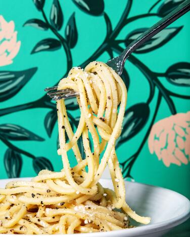 A fork lifts cacio e pepe pasta from a bowl