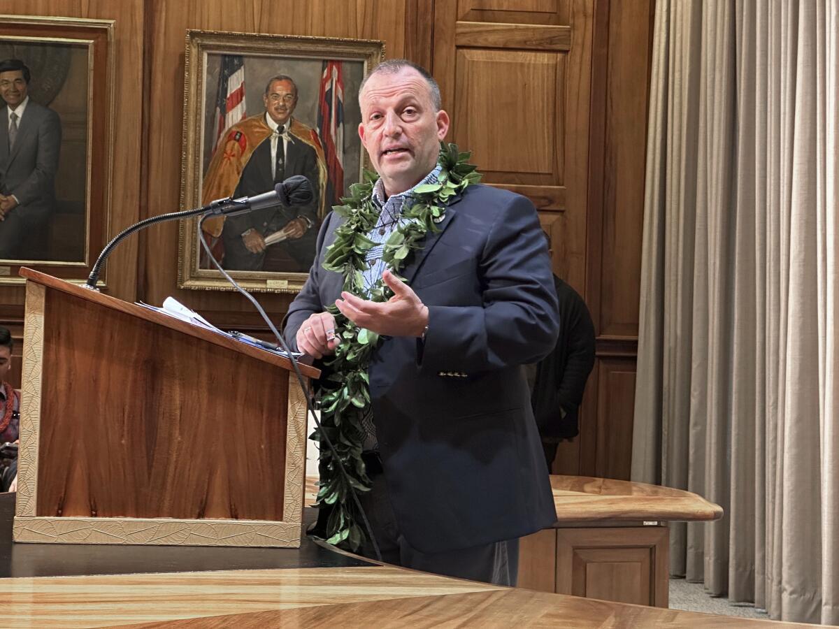 A man wering a suit and a lei stands at a podium. 