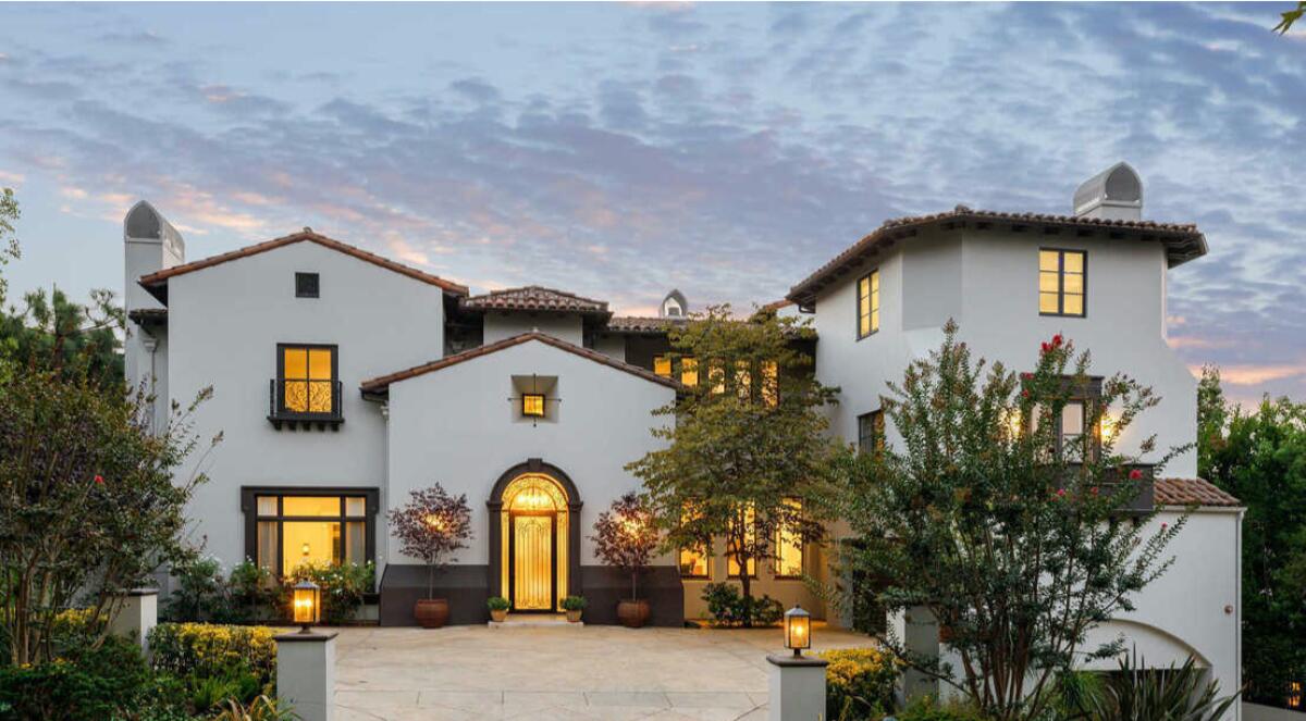 A two-story house with an arched front door, trees and plants