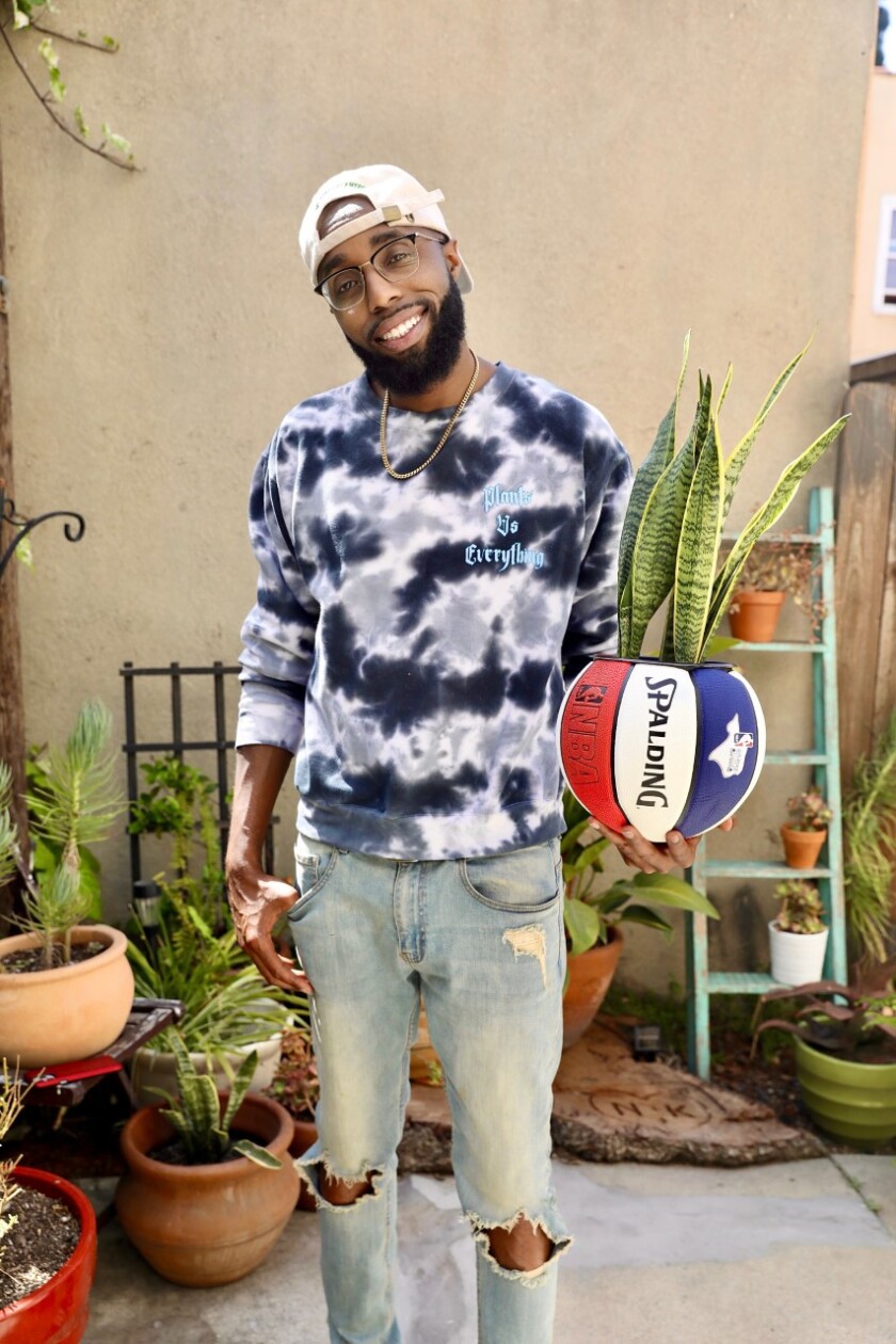 A man holds a red white and blue Spalding basketball planter with a snake plant inside.