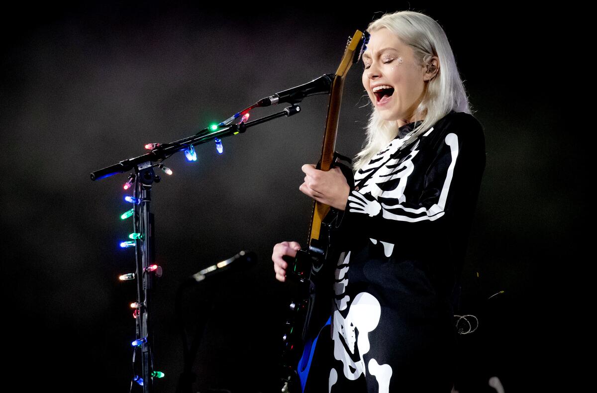A blond woman in a skeleton costume plays guitar and sings into a microphone.
