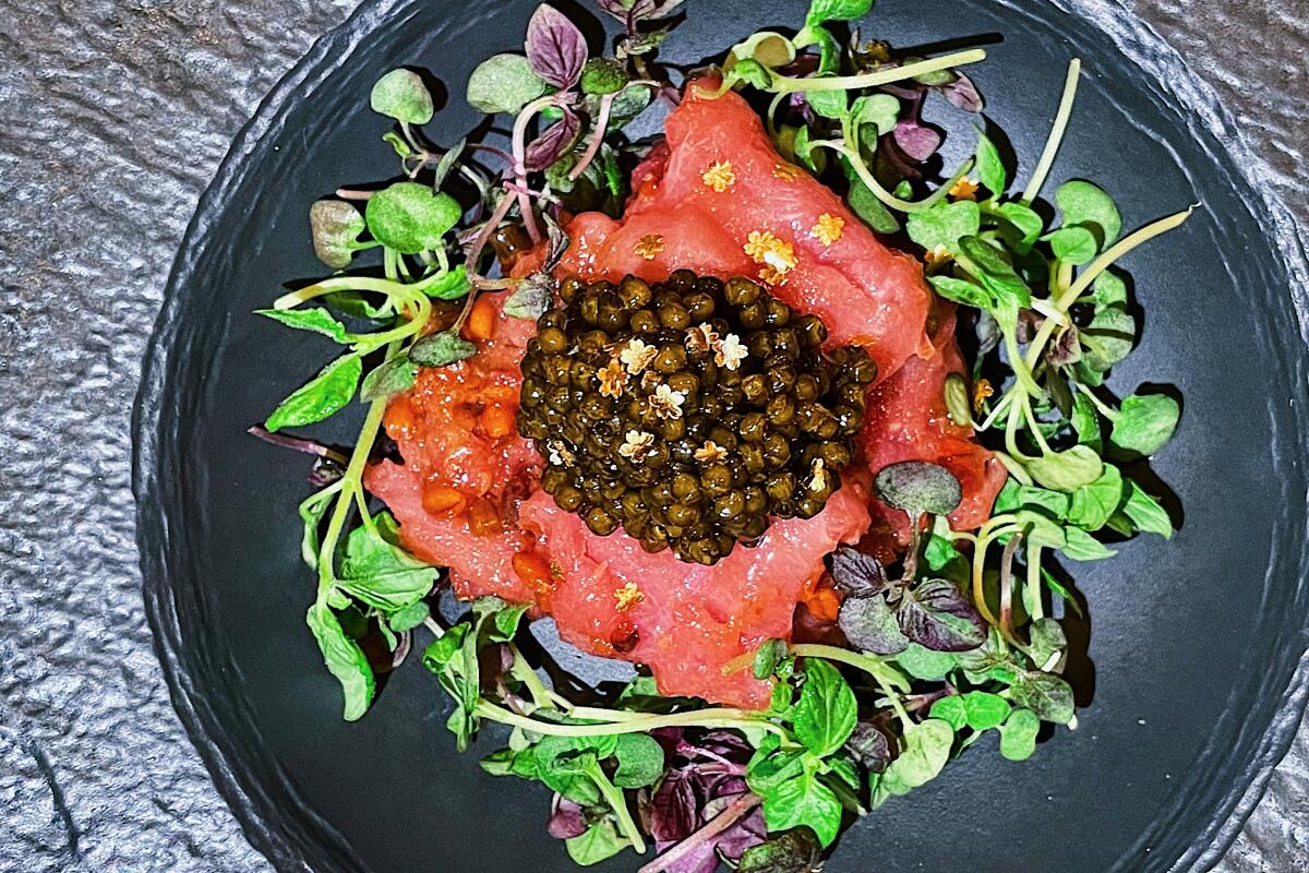 A mound of fatty bluefin tuna atop microgreens, all topped with a mound of caviar, on a black plate