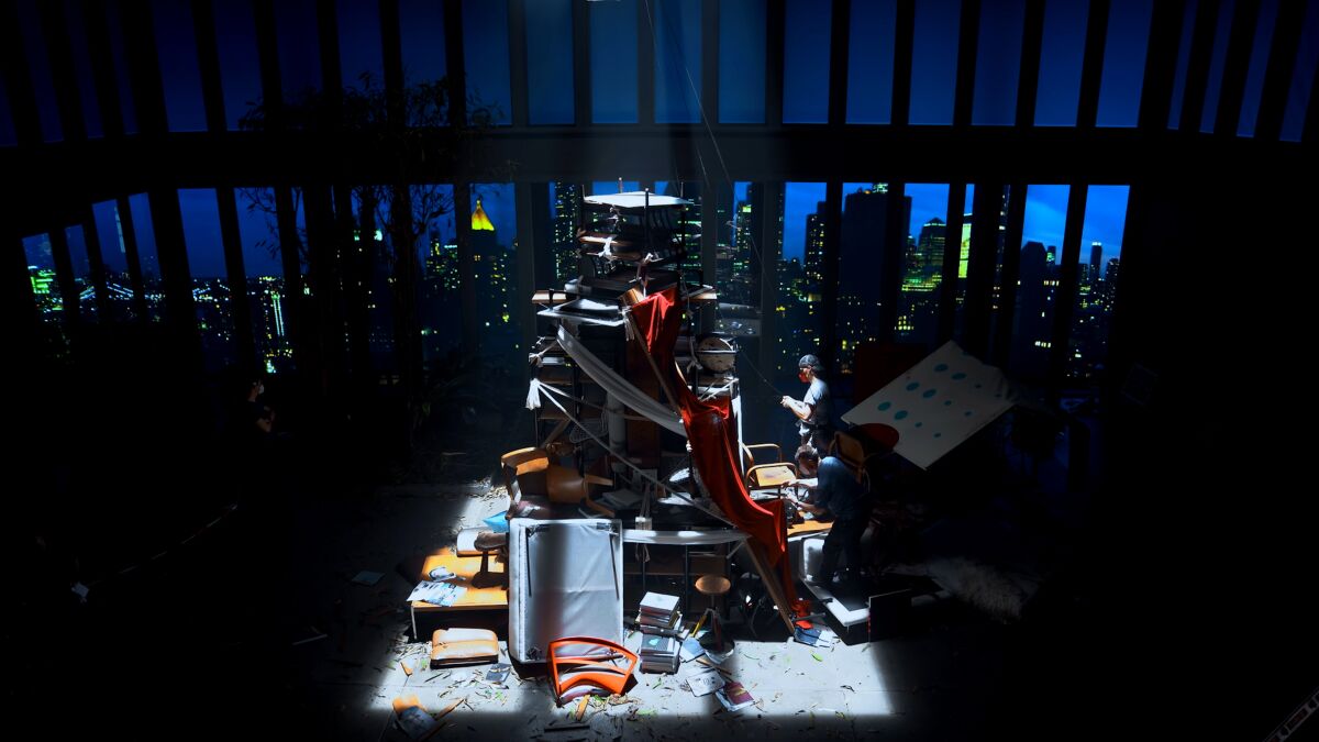 A crew building a darkly lit sculpture with a cityscape seen through windows.