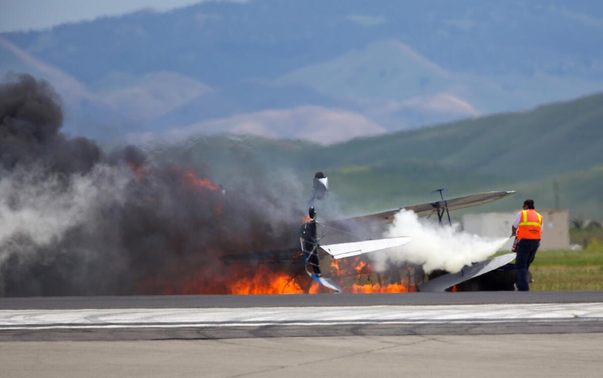 A worker fights a fire after a vintage biplane crashed upside-down on a runway at an air show at Travis Air Force Base in Fairfield, Calif., Sunday, May 4, 2014. The pilot, Edward Andreini, 77, of Half Moon Bay, was killed.