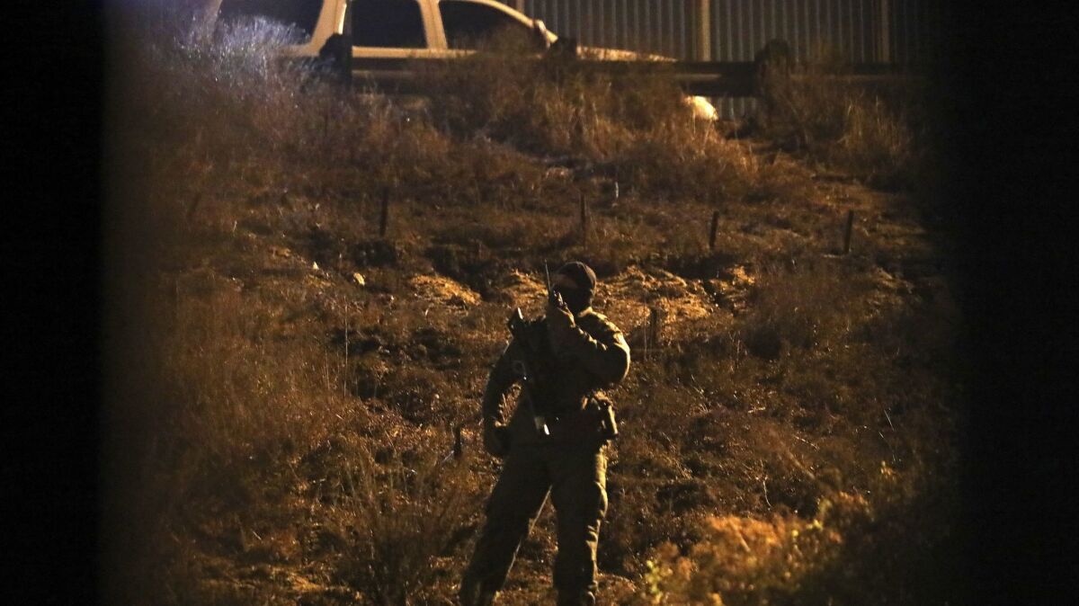 A U.S. Border Patrol agent keeps an eye on a group of Honduran migrants standing near the border wall as seen from Tijuana on Friday, Nov. 30. The group eventually crossed and was immediately detained.