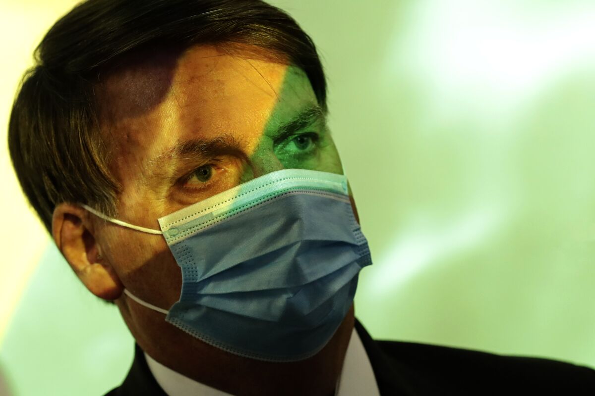 Brazil's President Jair Bolsonaro wears a mask amid the COVID-19 pandemic at the start of a ceremony where his nation's flag is projected in Brasilia, Brazil, Wednesday, Aug. 5, 2020. (AP Photo/Eraldo Peres)