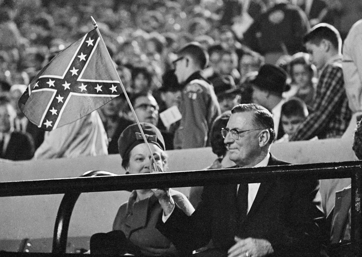 FILE - Mississippi Gov. Ross Barnett waves a confederate flag before the start of Ole Miss-Kentucky football game at the stadium on Sept. 29, 1962, in Jackson, Miss. With Barnett is his wife, the former Pearl Crawford, left. Mississippi in 2022 is on the verge of retiring a state song with racist roots, two years after it surrendered a Confederate-themed state flag. “Go, Mississippi" uses the tune of a 1959 campaign song for Ross Barnett, who won the governor's race proclaiming support of segregation. (AP Photo/Jim Bourdier, File)