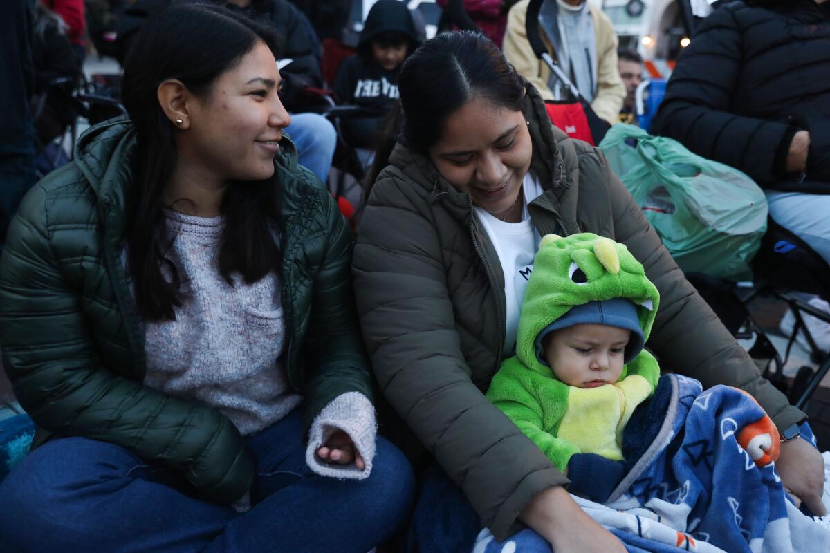 Two women and a child wait in the brisk morning, for the start of the Rose Parade.