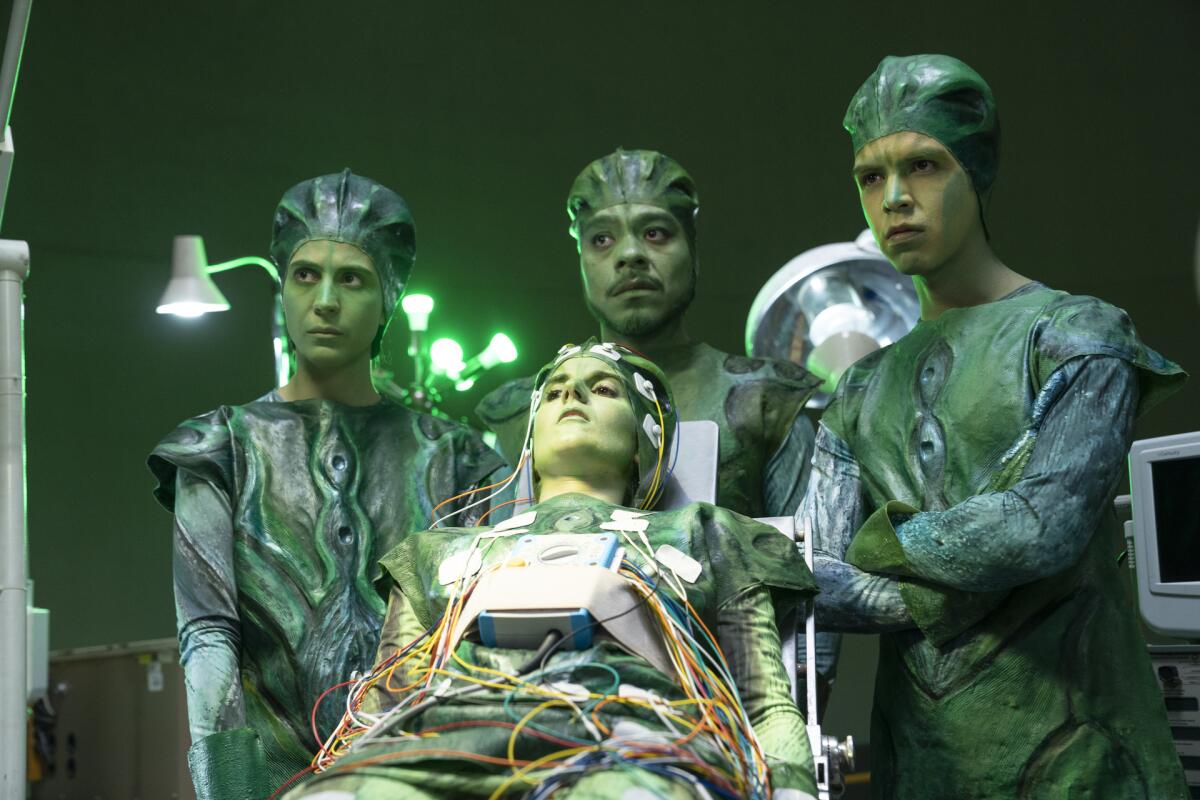 A scene from Los Espookys shows the cast dressed up as green aliens inside a lab
