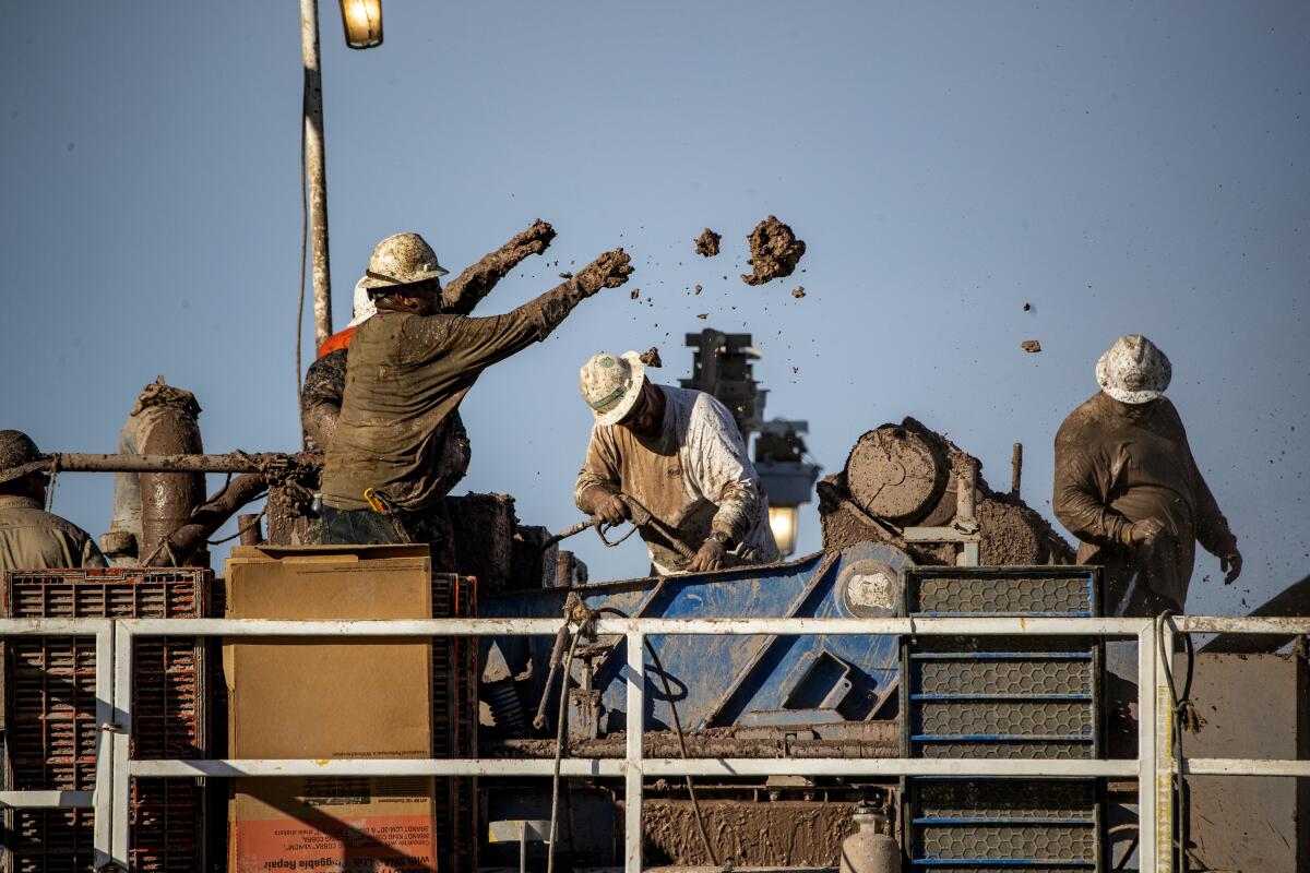 Workers remove clay from machinery.