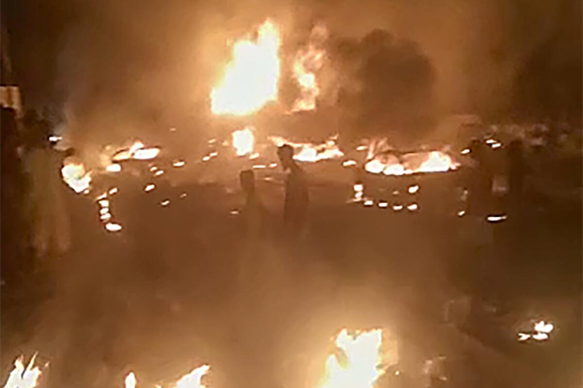 People walk by burning debris following the explosion of an oil tanker