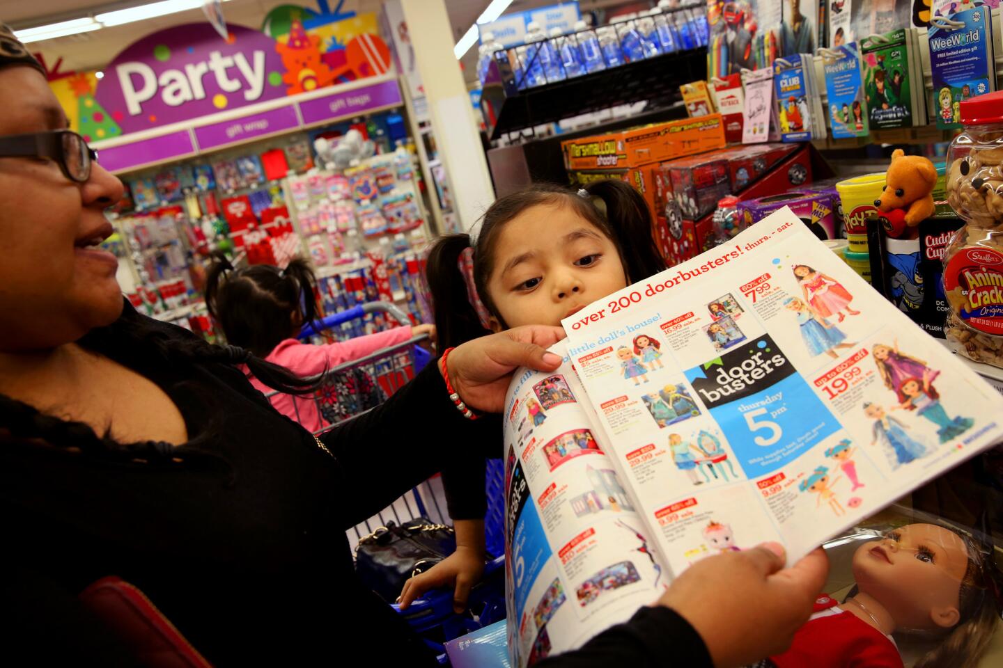 Jakayla Guerrero, 5, peers over the top of the sales flier her mother, Laura Morales, of Los Angeles, shows a Toys R Us cashier at the checkout lane to confirm a sale item on Black Friday.