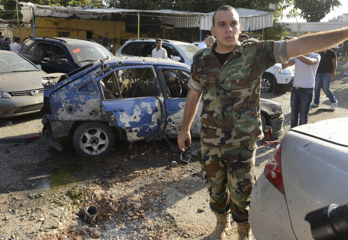 A Lebanese army officer stands next to a damaged car as he asks journalists to step back from the scene where a rocket struck a used car lot at the Mar Mikhael district of south Beirut on Sunday.