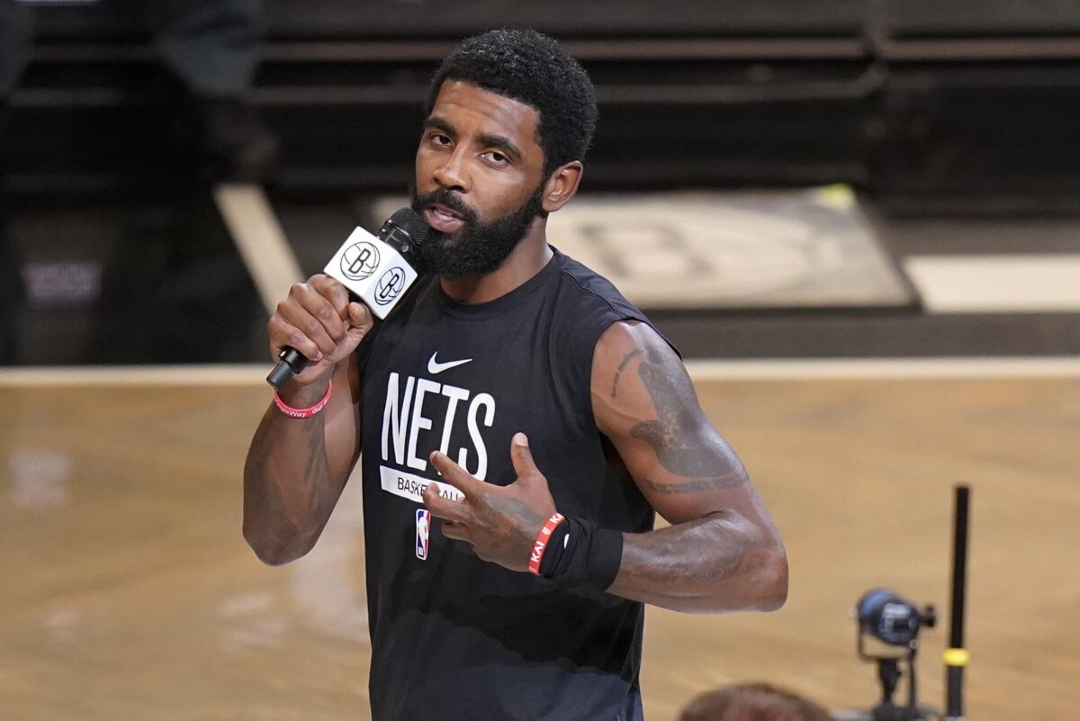 The Brooklyn Nets' Kyrie Irving holds a microphone and speaks on the court.
