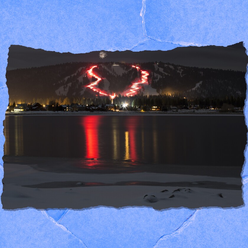 Ribbons of light on a snowy mountain are reflected in a lake at night.