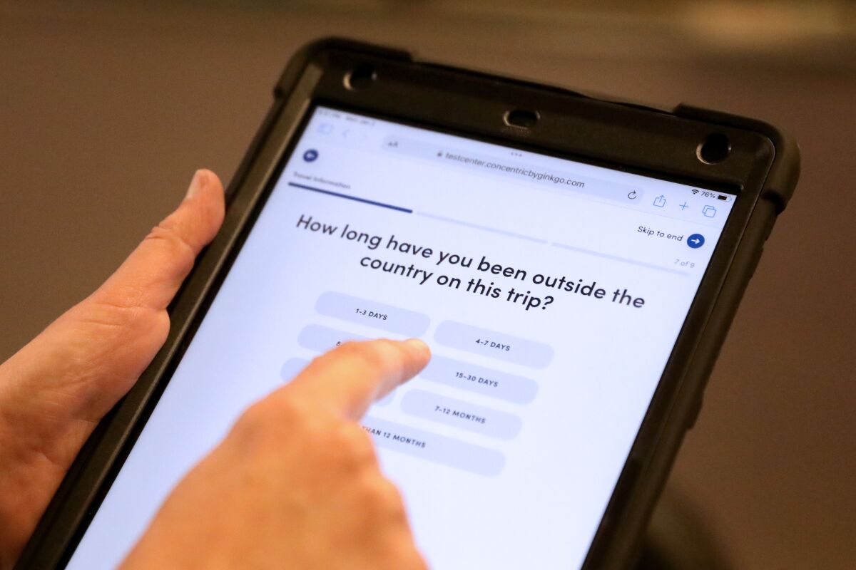 A worker holds a digital tablet with questions for airline passengers arriving from overseas.